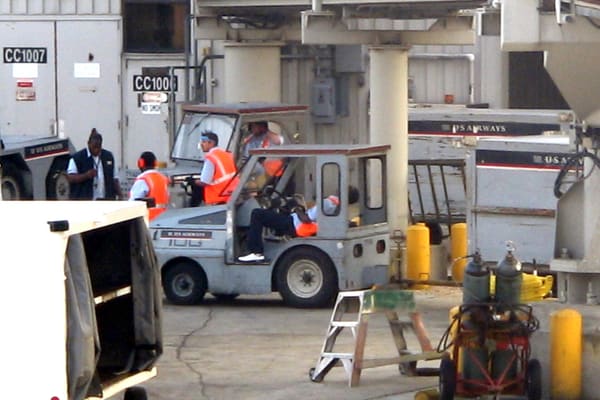 Ground crew work an aircraft at a gate. Bag and seat fees now appear alongside the fare.